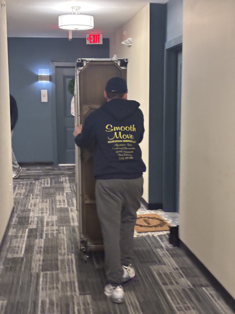 Professional mover from Smooth Move Relocation Services transporting furniture on a dolly inside a Mason Ohio apartment hallway during a residential move.