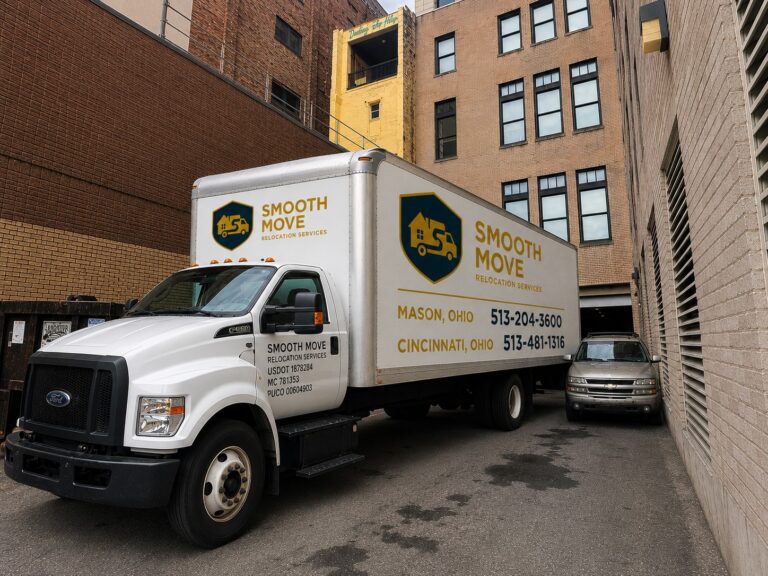 A Smooth Move Relocation Services moving truck parked in downtown Cincinnati between commercial buildings during a professional residential and commercial relocation. The truck displays the company’s Mason and Cincinnati office phone numbers along with USDOT 1878284, MC 781353, and PUCO 00604903, highlighting local and long-distance moving services throughout Greater Cincinnati.